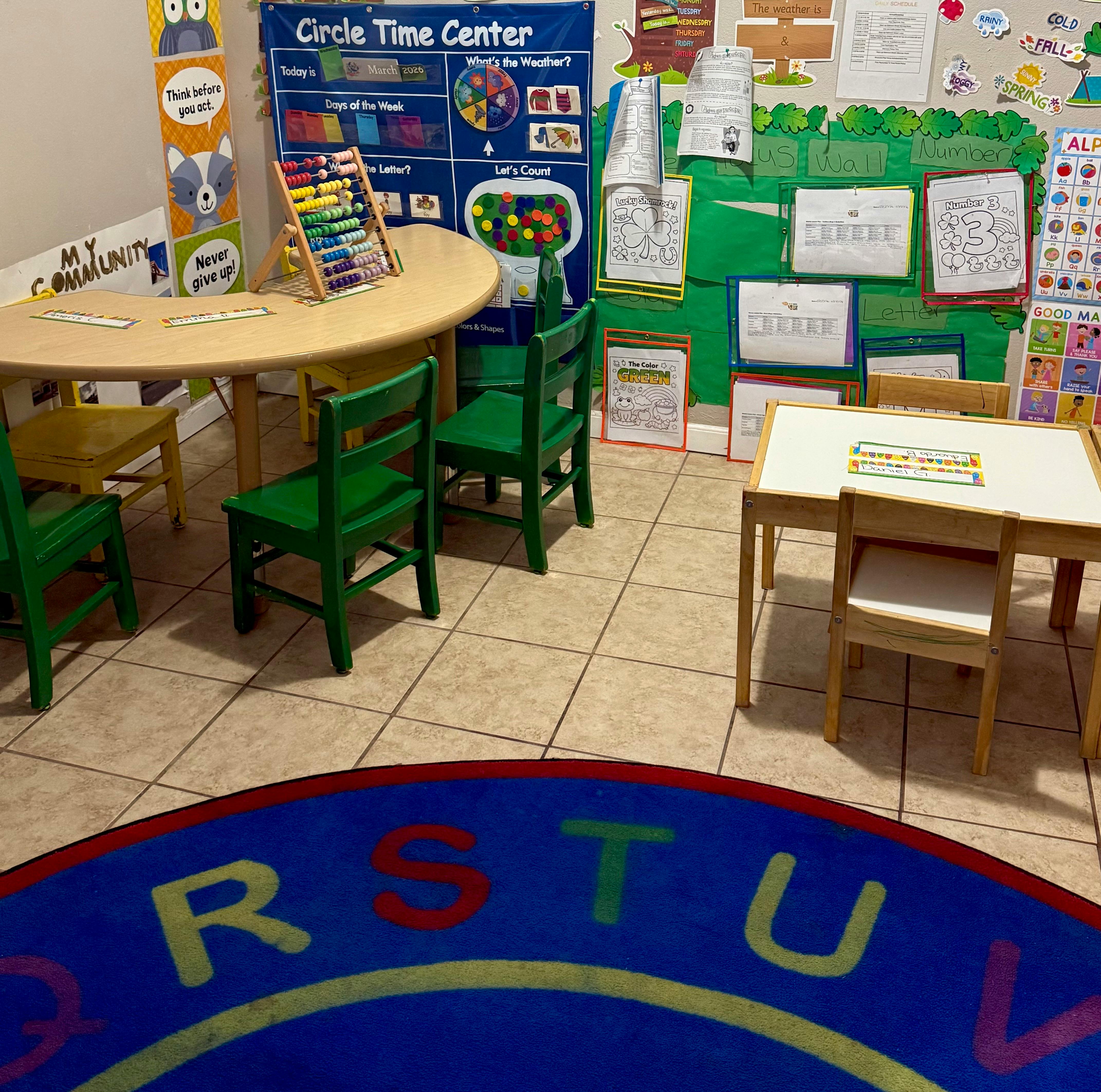 Classroom with child-sized tables and chairs, a blue rug with alphabet letters, and wall displays
