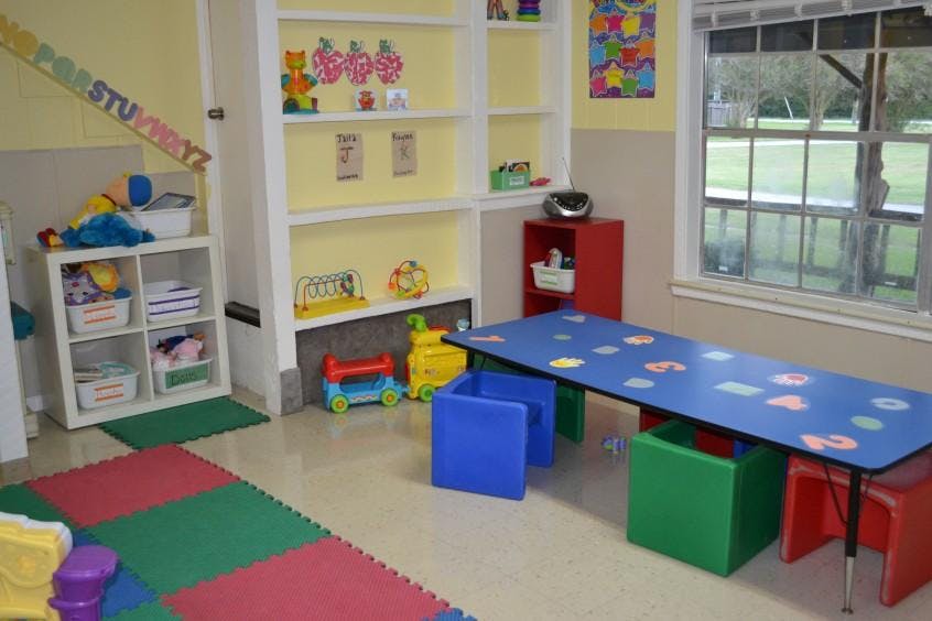 Playroom with shelves of toys, a long table with chairs, and a window
