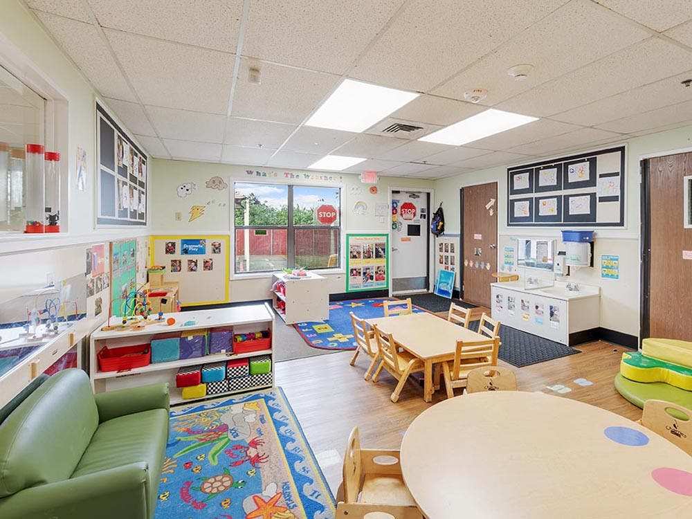 Colorful classroom with small tables and chairs, a green couch, and cubbies