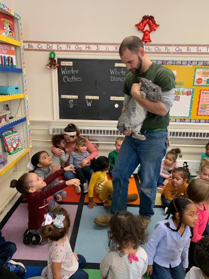 Person holding a rabbit in front of children in a classroom