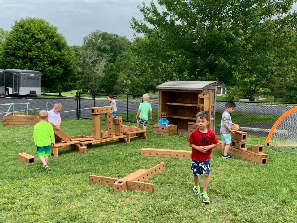 Children playing with large wooden blocks on a grassy area