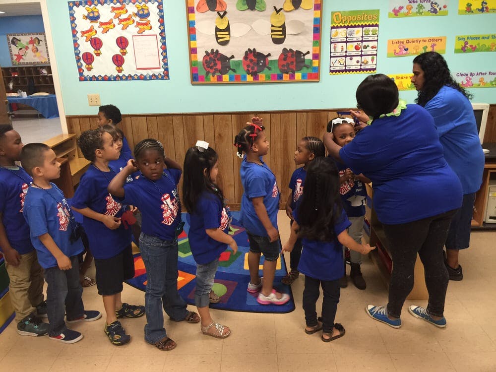 Adults helping children in blue shirts in a classroom