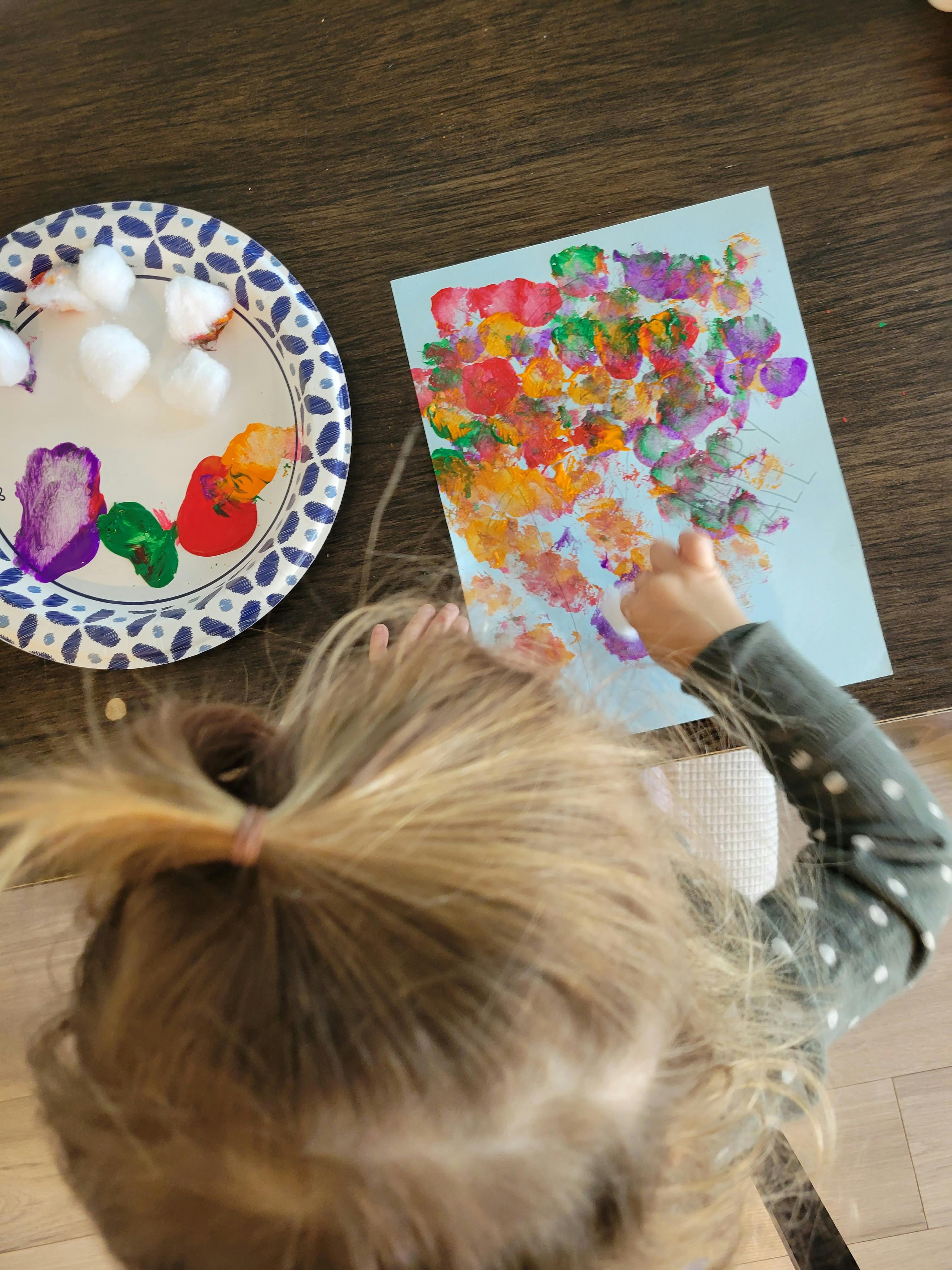 Child painting on paper using cotton balls and paint on a paper plate