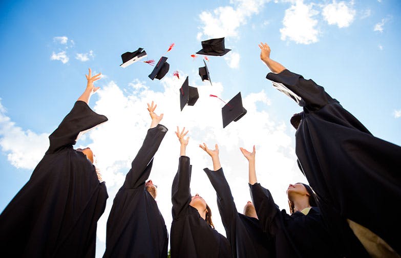 Group of people in graduation robes throwing caps into the air