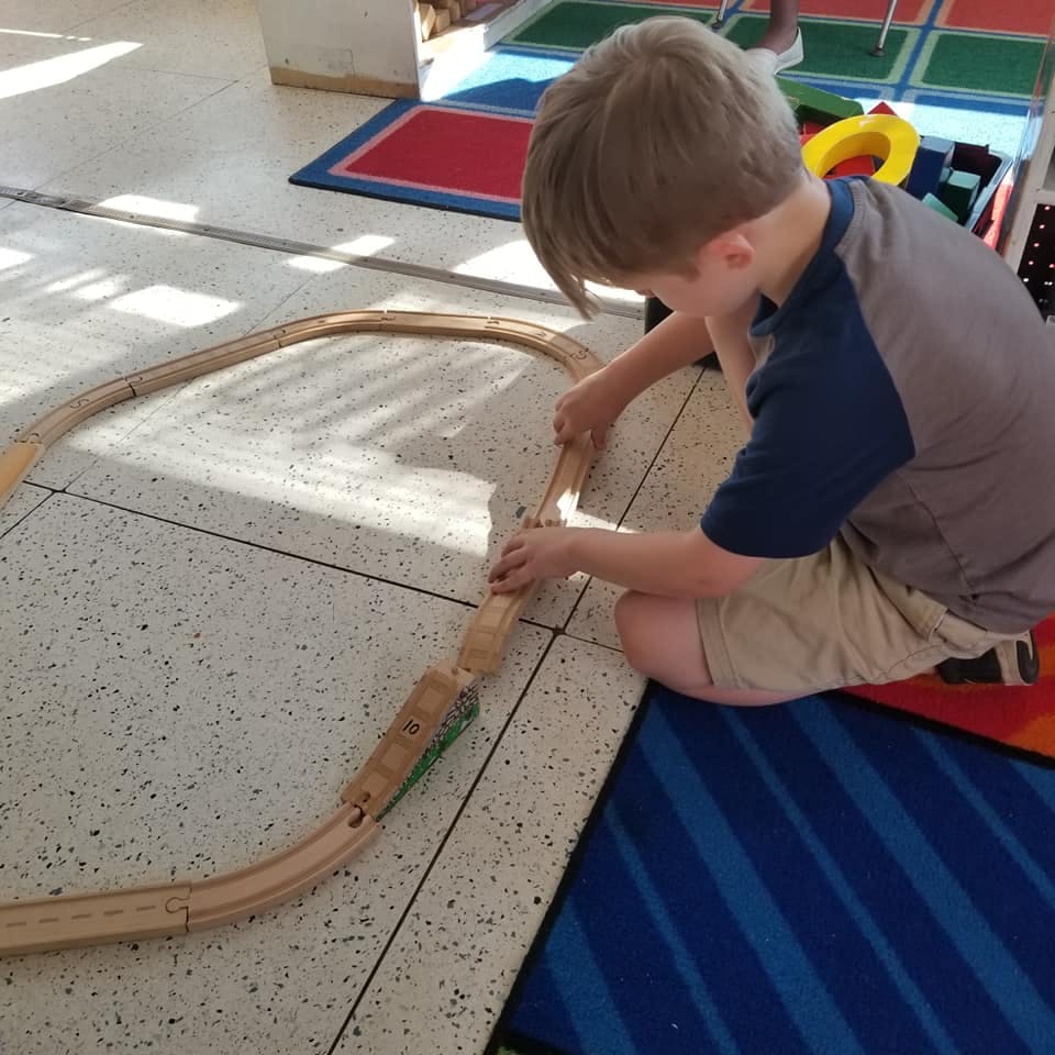 Child playing with wooden train tracks on the floor
