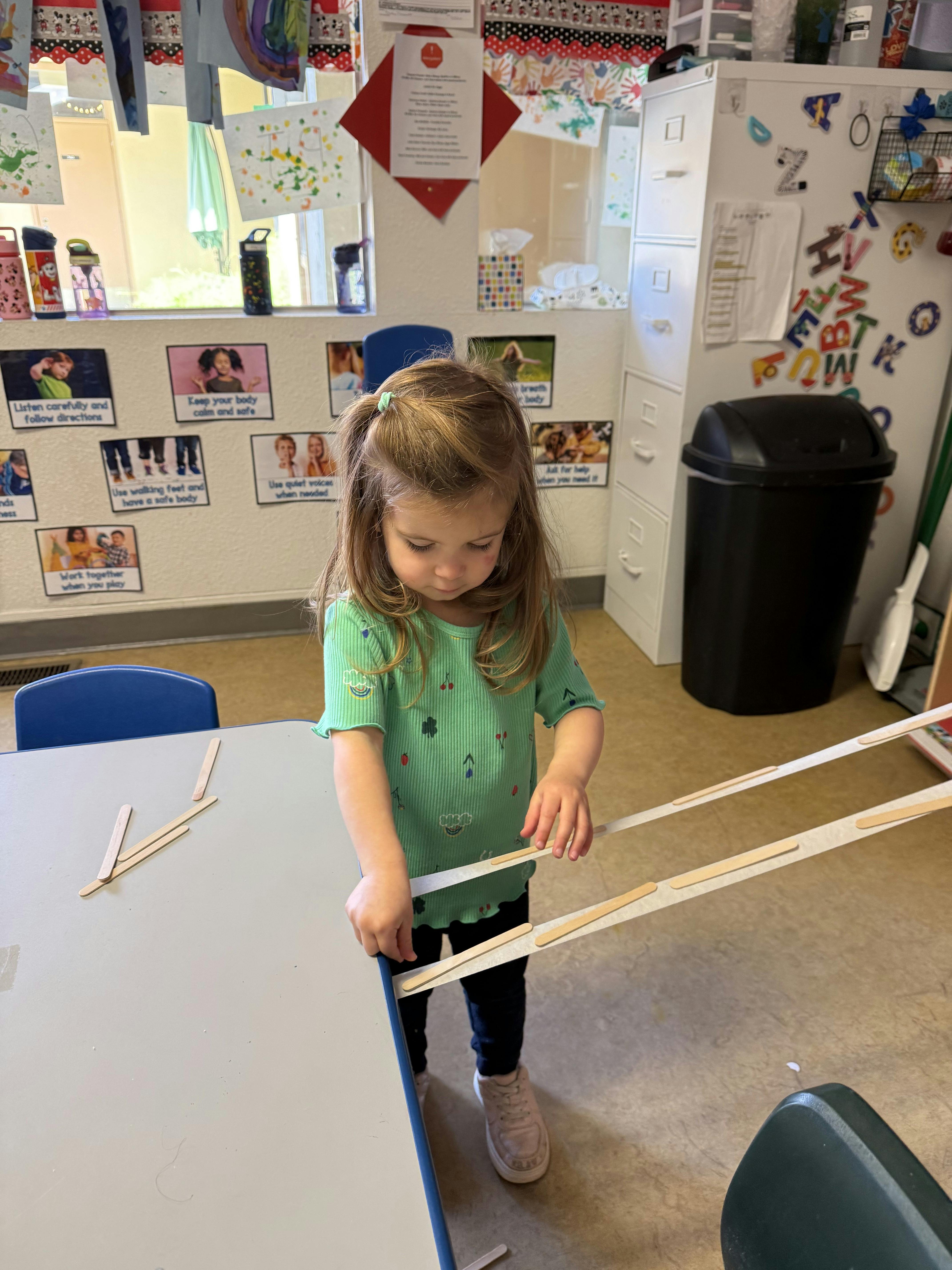 Child building with craft sticks on a table in a classroom