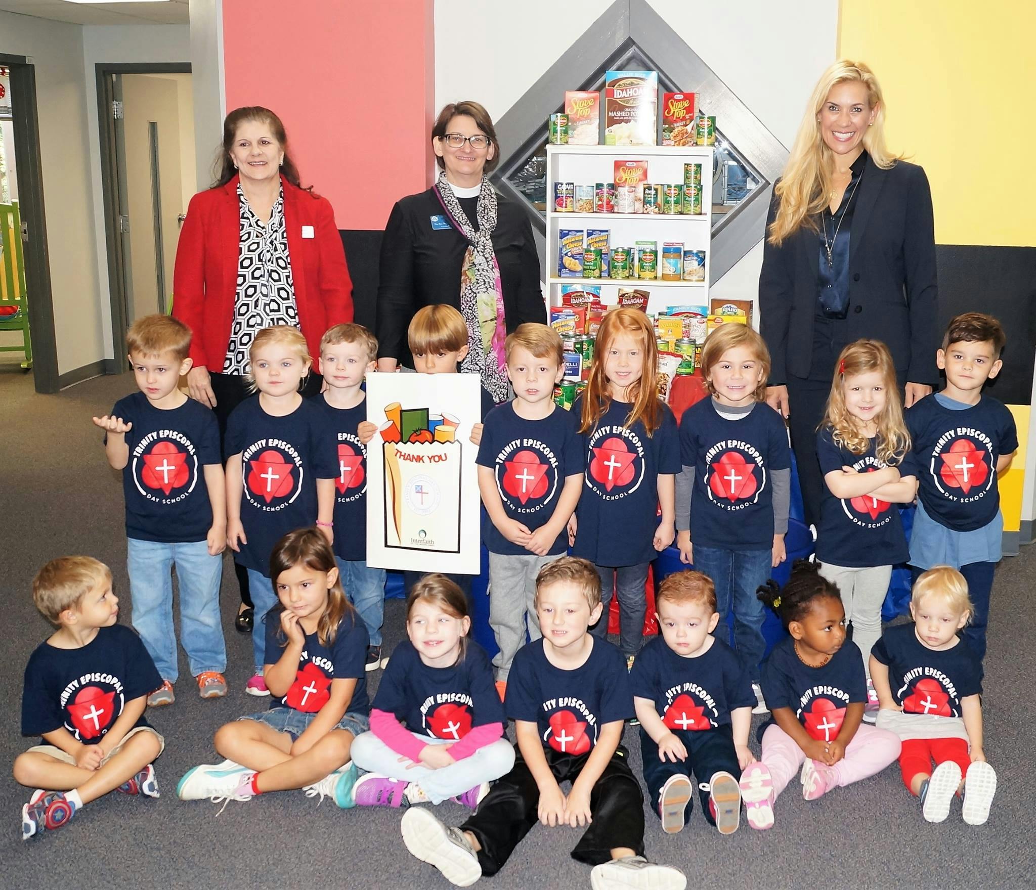 Three adults and many children in matching shirts posing in front of shelves