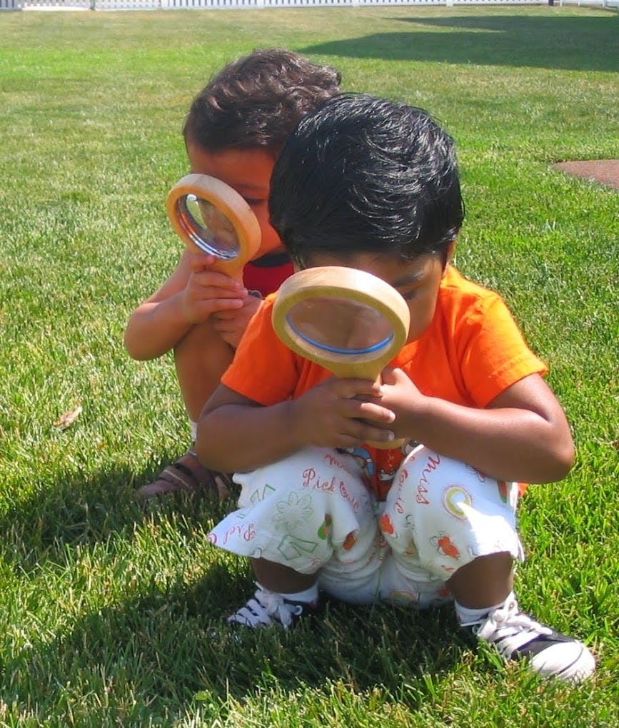 Two children crouching in grass, looking through magnifying glasses