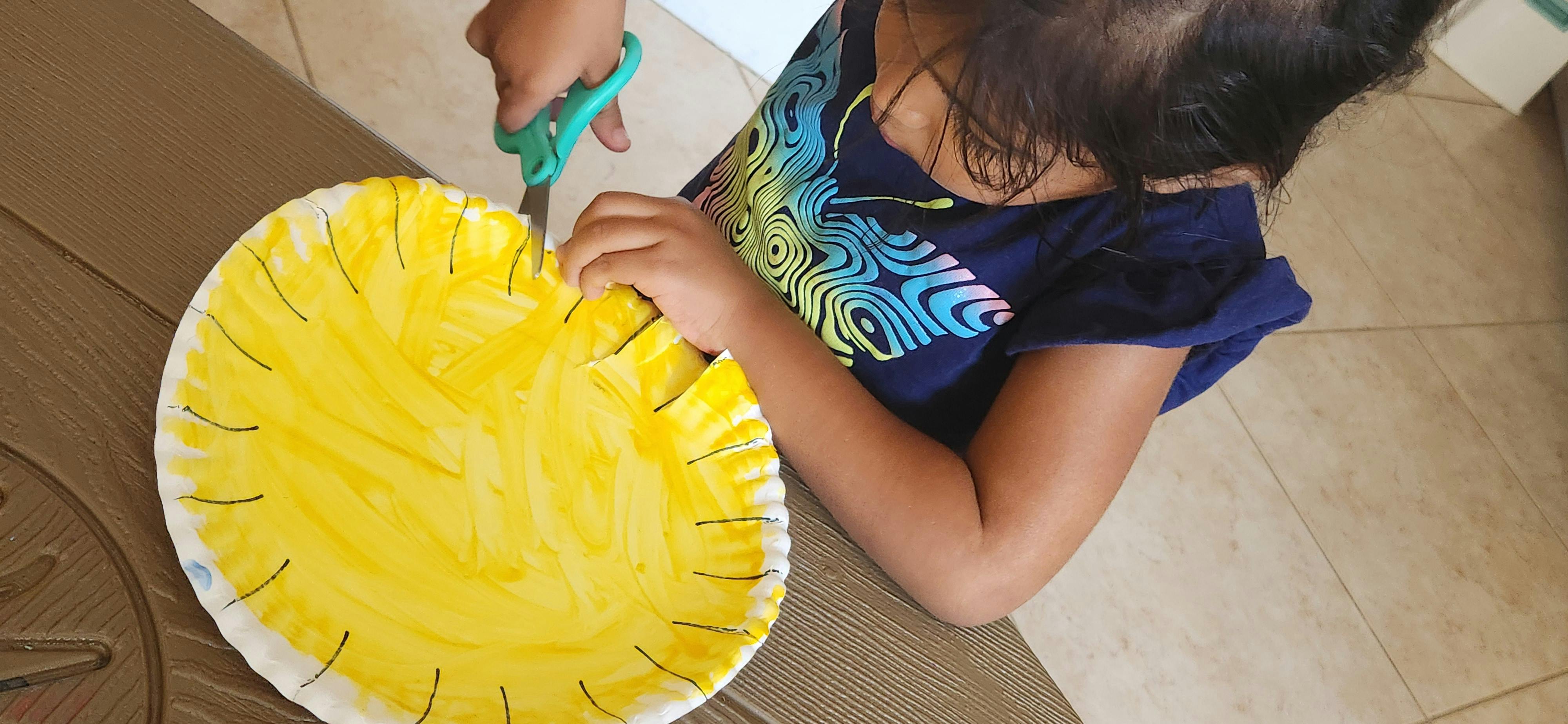 Child cutting a yellow paper plate with scissors