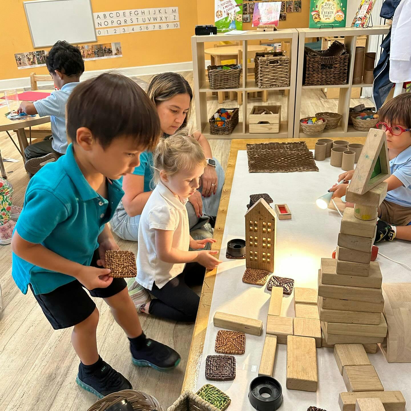 Children and a person playing with wooden blocks and building toys in a classroom