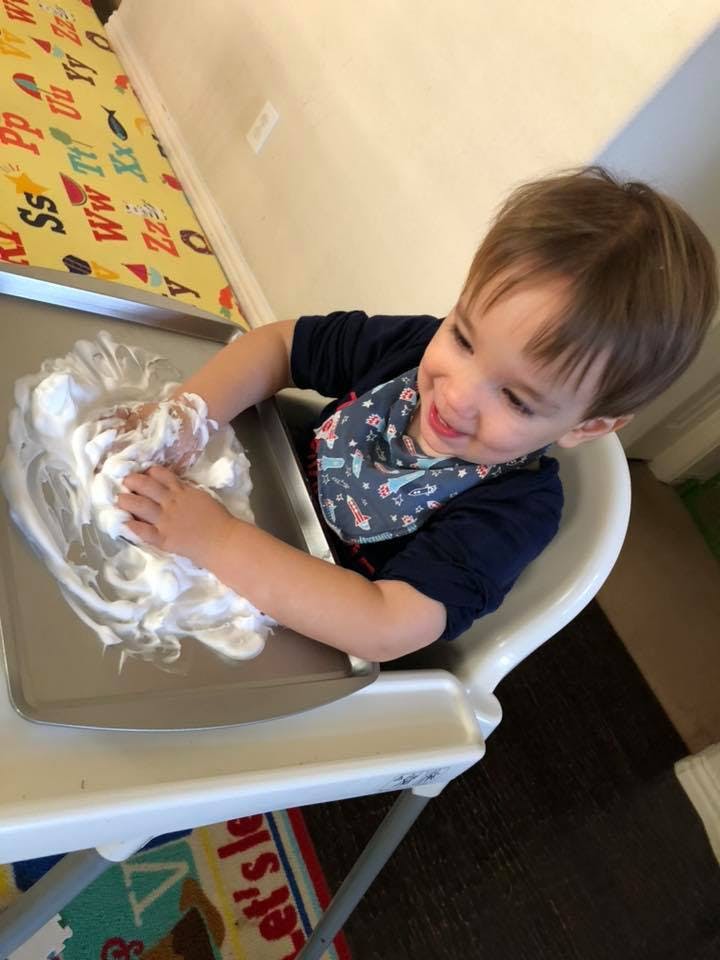 Child in high chair playing with shaving cream