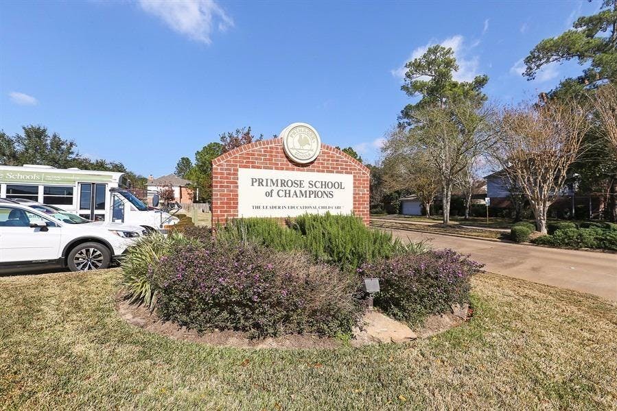 Brick sign for Primrose School of Champions with cars and trees
