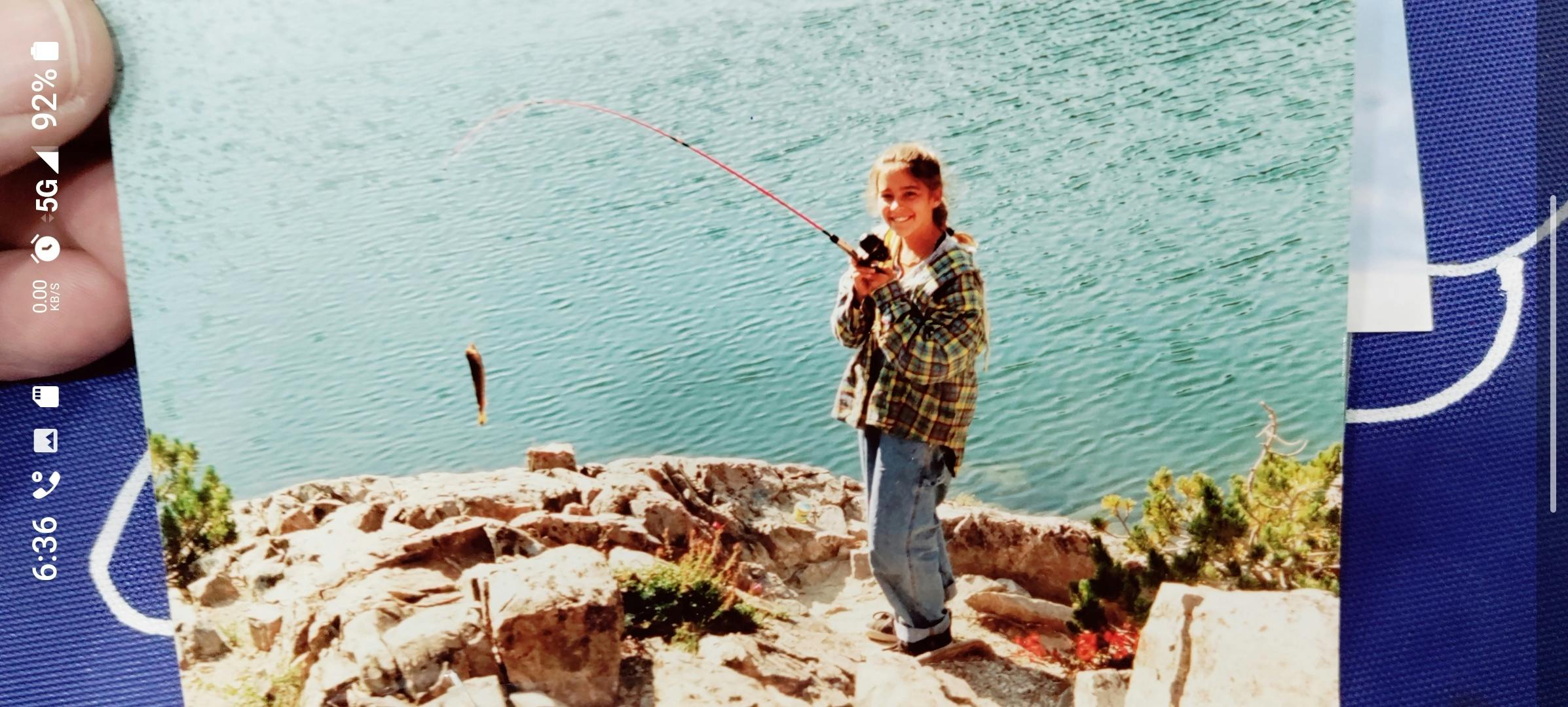 Child on a rocky bank holding a fishing pole with a fish on the line over water