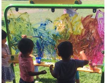 Children painting on a clear easel outdoors
