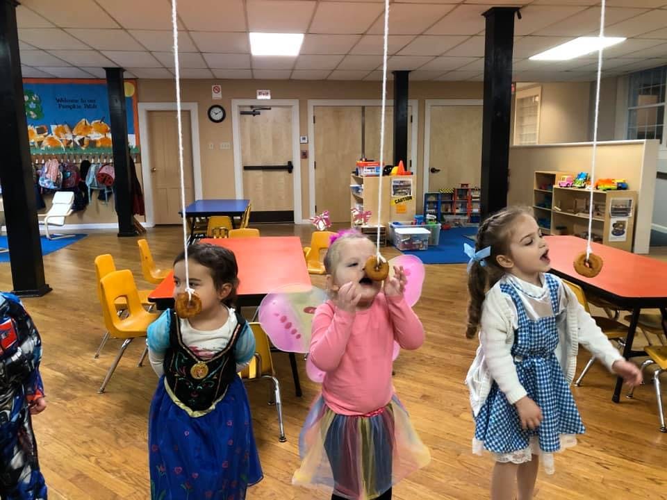 Three children playing a game with donuts on strings in a classroom