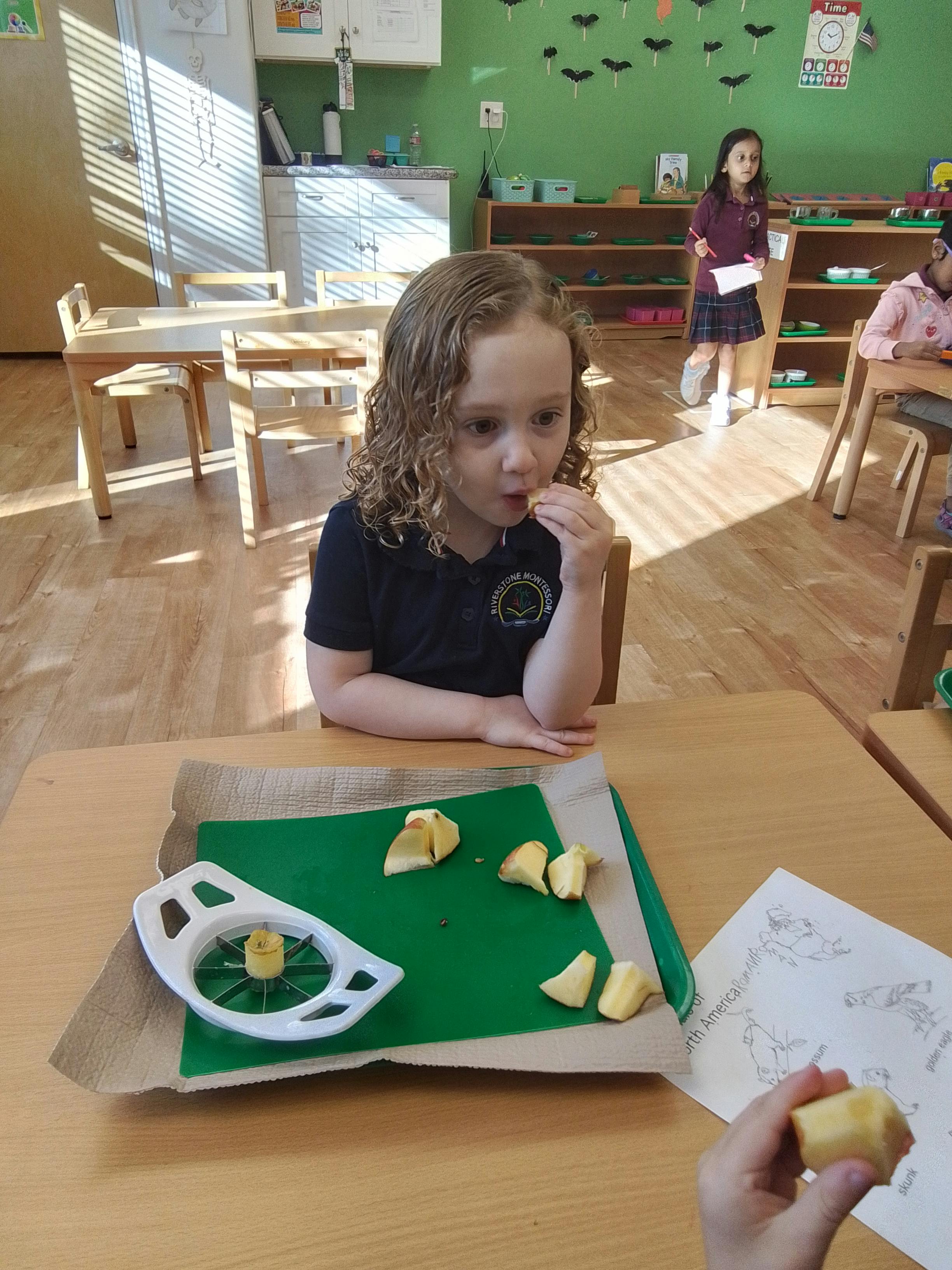 Child eating apple slices at a table in a classroom