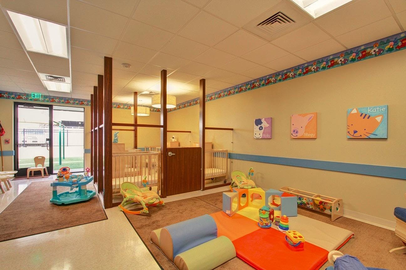 Daycare room with play mats, toys, and cribs