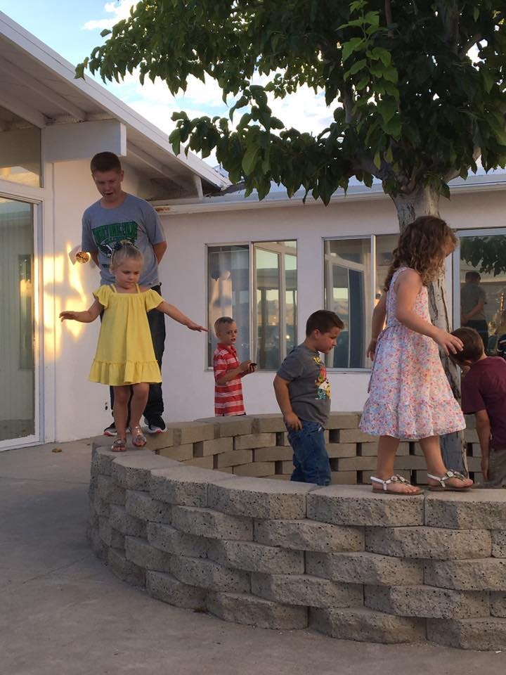 Children playing on and around a low stone wall outdoors