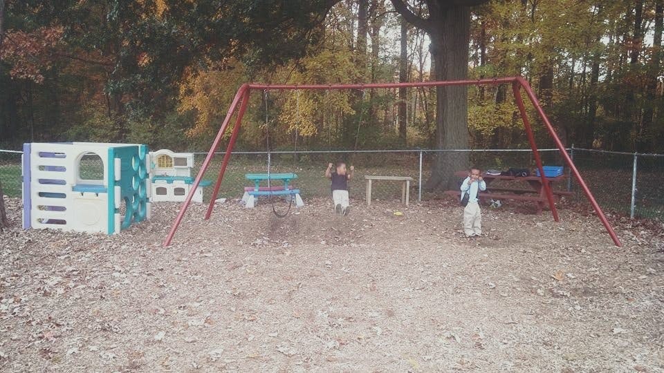 Two children on a playground with a swing set and playhouses