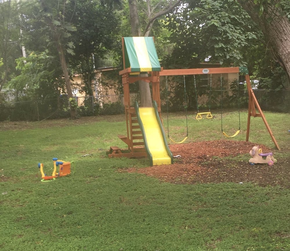Wooden playset with yellow slide and swings in a grassy yard