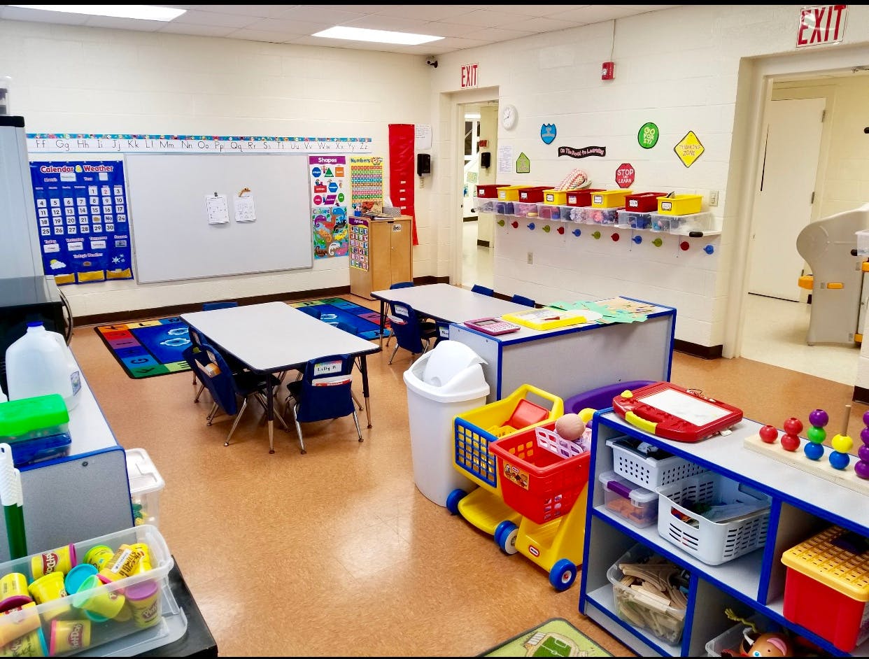 Empty classroom with small tables and chairs, whiteboard, and colorful learning materials