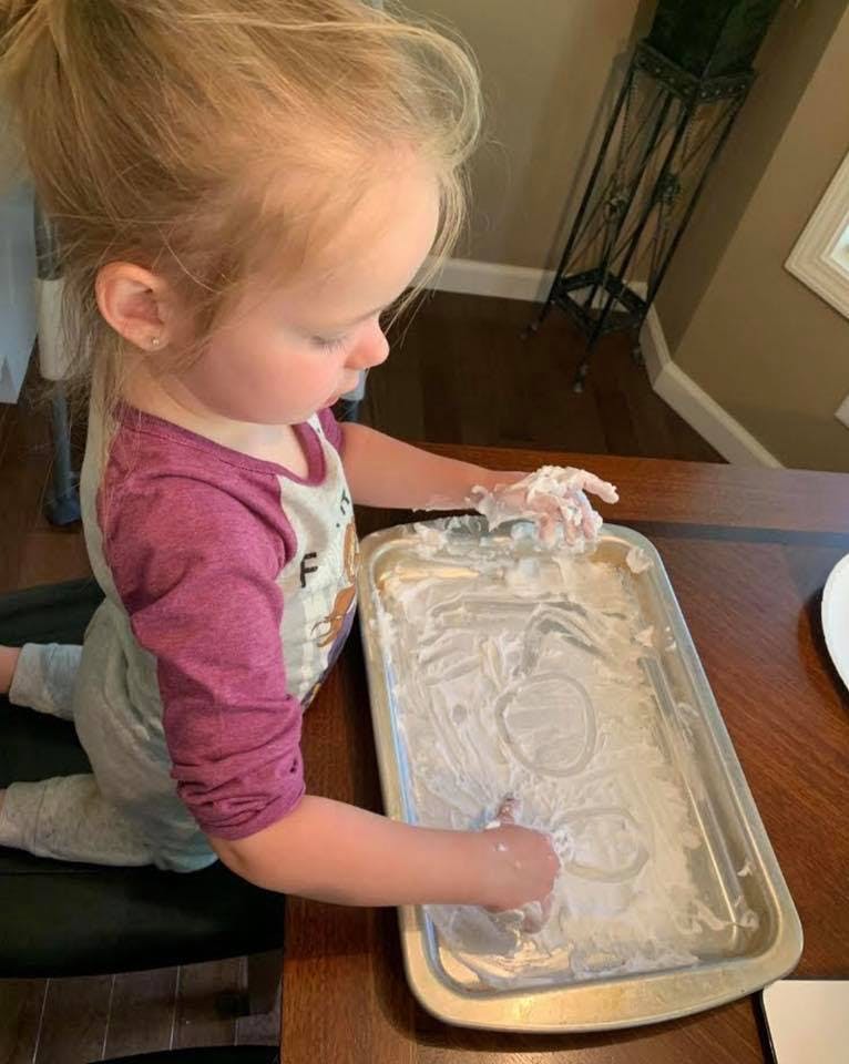 Child playing with shaving cream in a baking pan