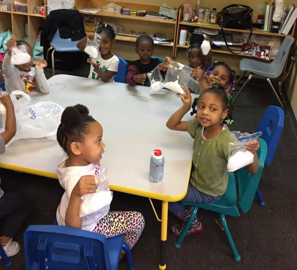 Children sitting at a table holding bags of white material