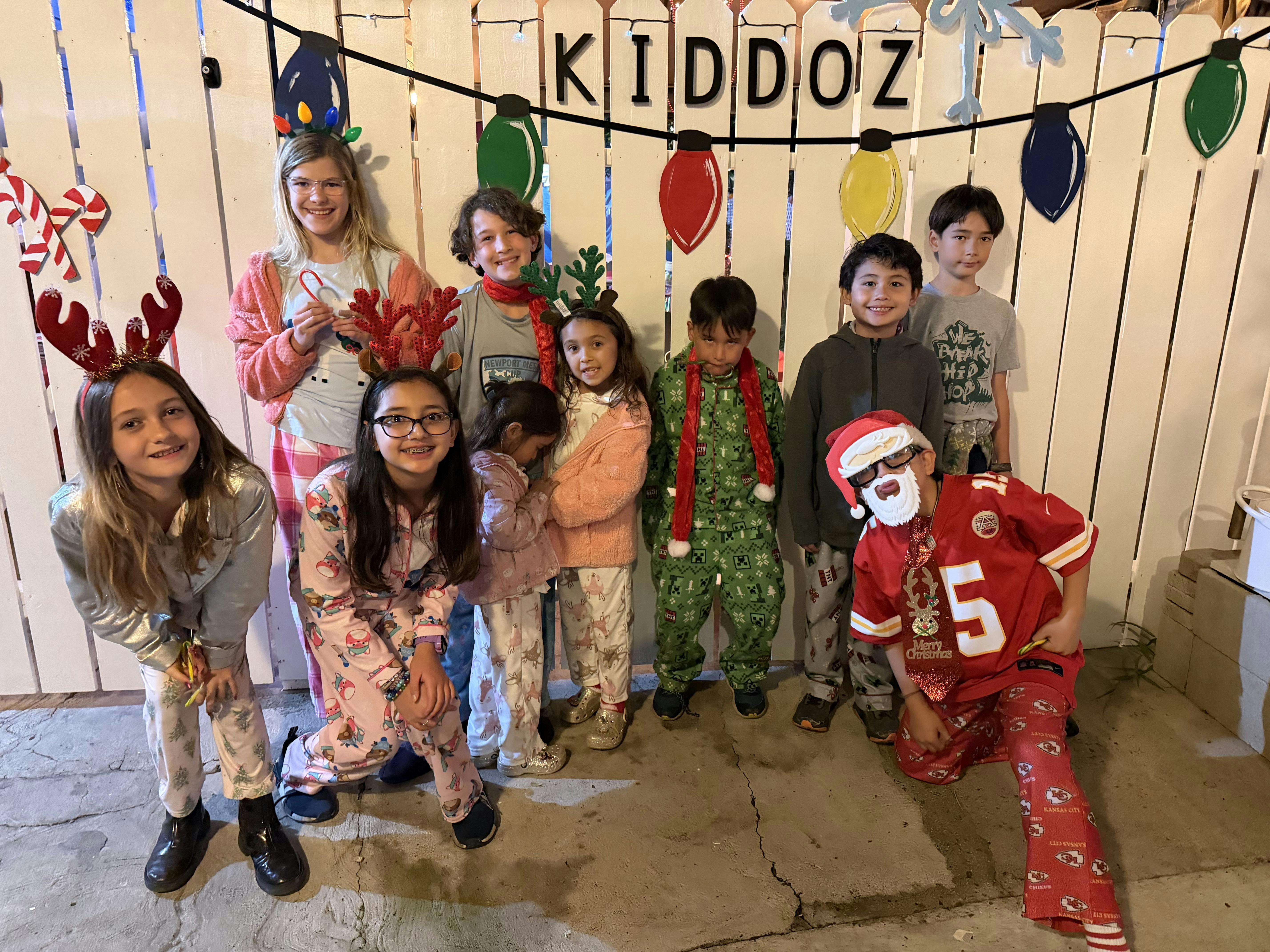 Group of children wearing pajamas and Christmas-themed headbands in front of a fence