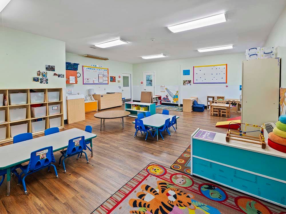 Empty classroom with small tables and chairs, shelves, and a colorful rug