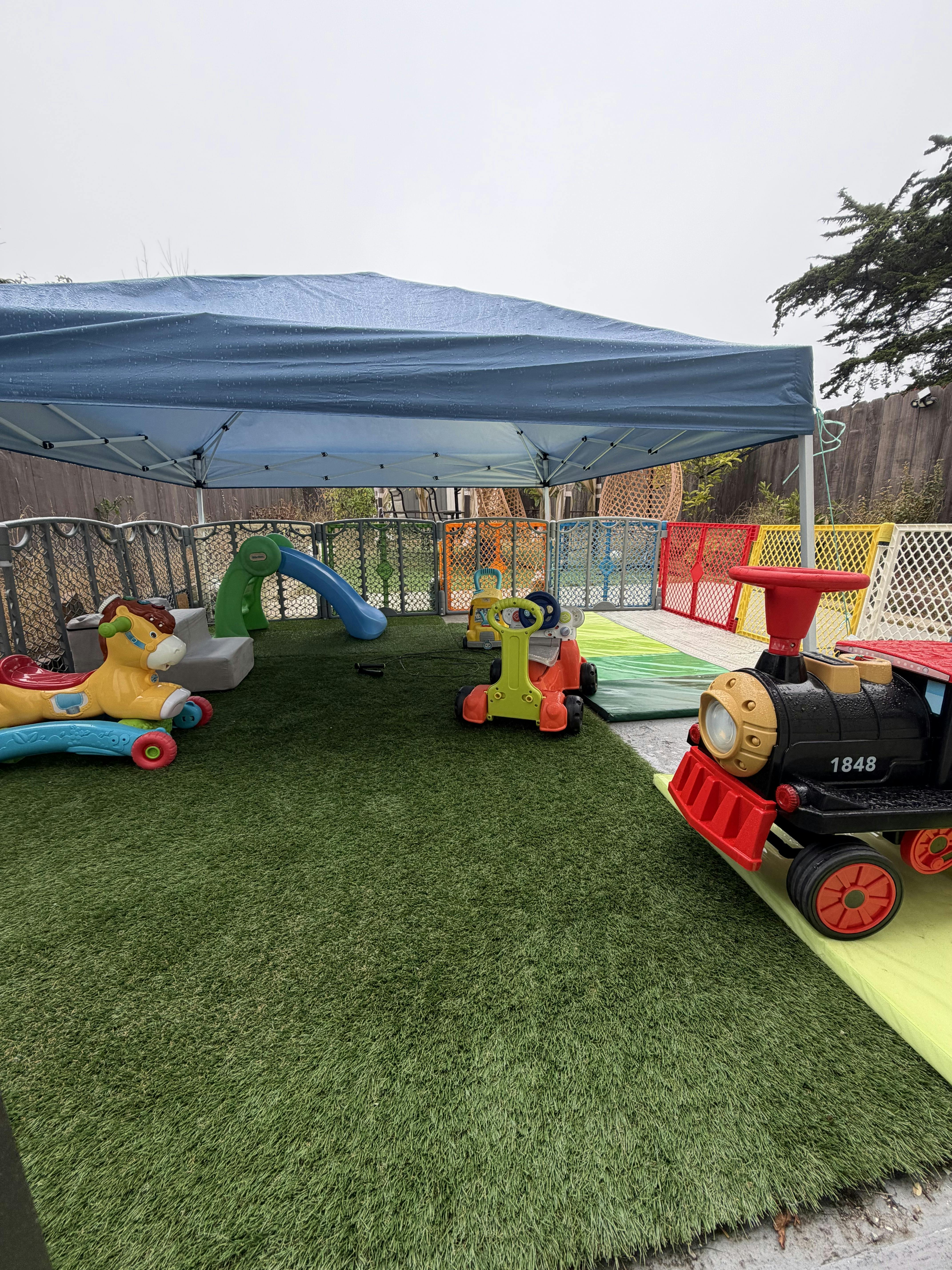 Plastic toy vehicles and slide on artificial turf under a blue canopy