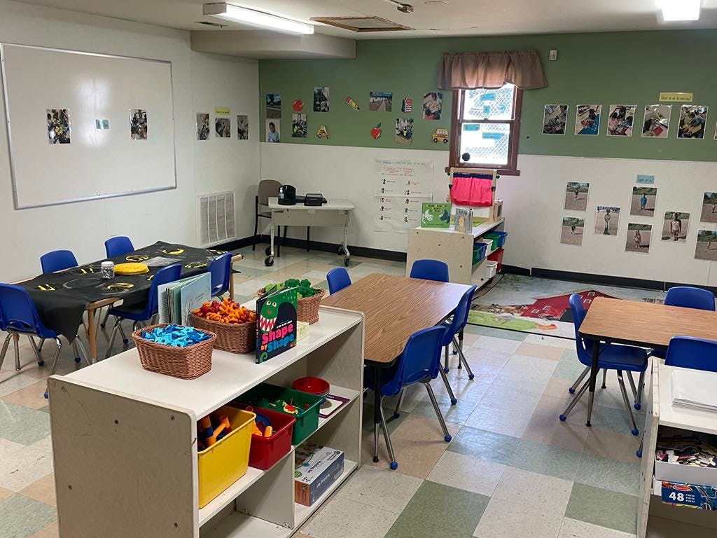 Classroom with small tables and chairs, toys, and pictures on the walls