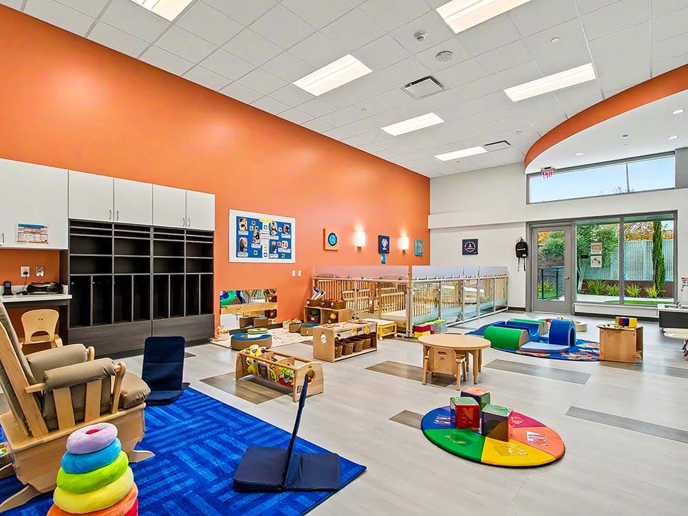 Empty colorful playroom with cribs, chairs, and play mats