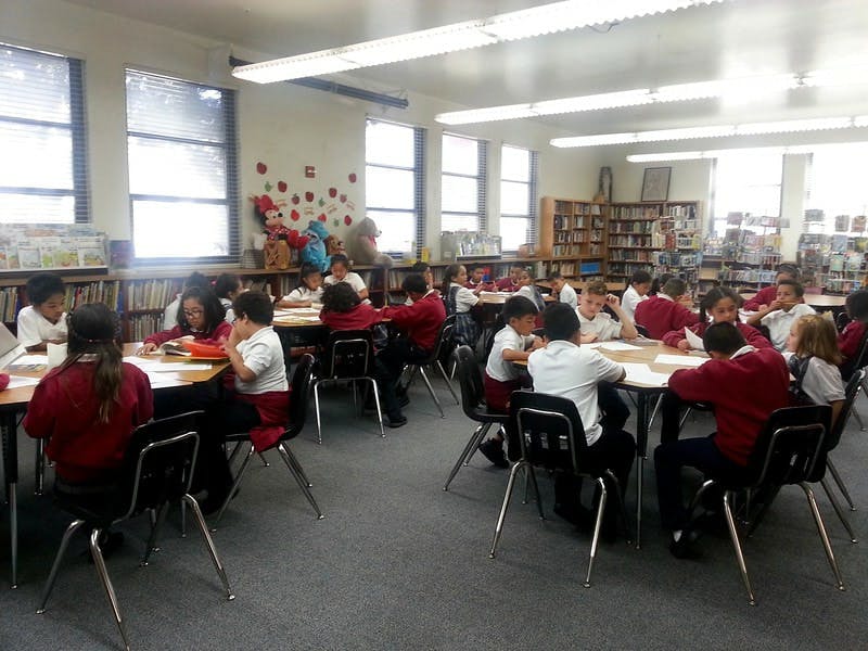 Group of children in school uniforms sitting at round tables in a library