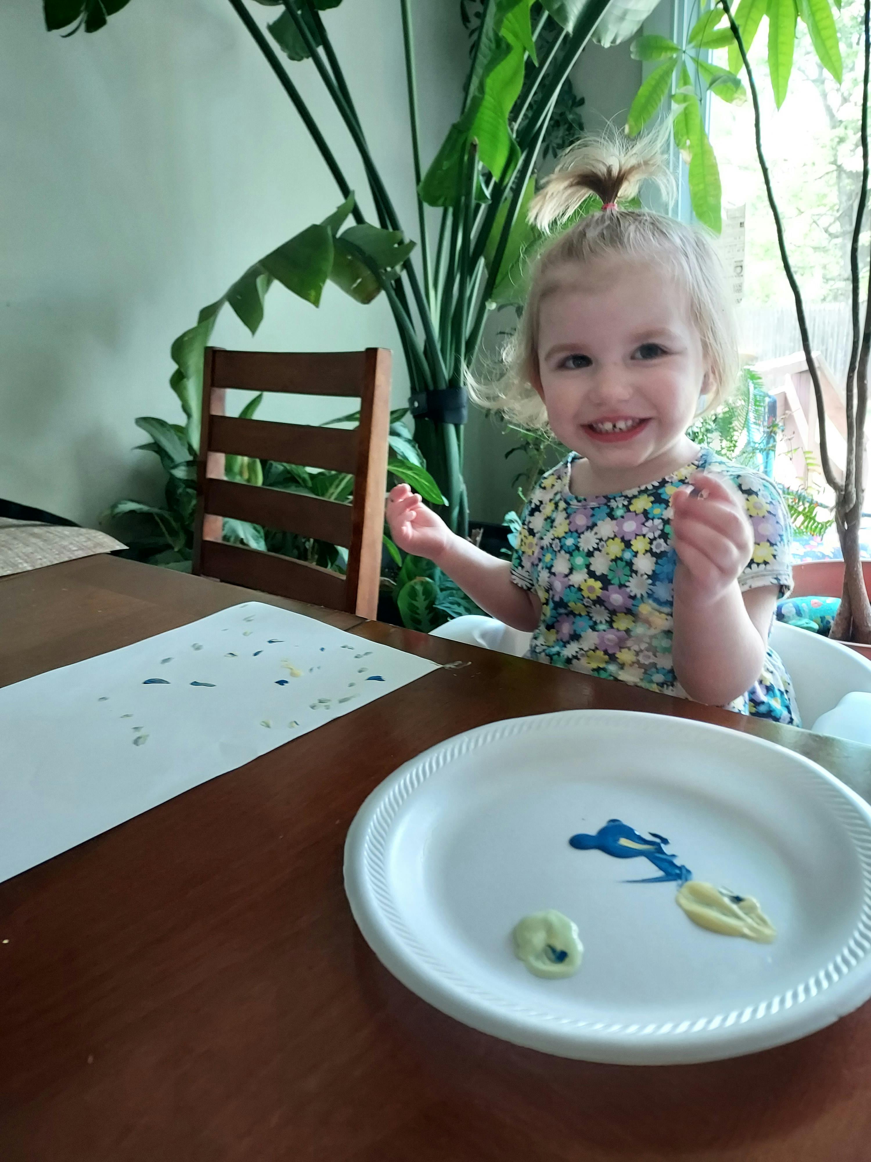 Child sitting at a table with paint on a plate and paper