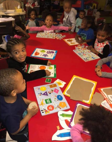 Children sitting around a red table with puzzles and learning games