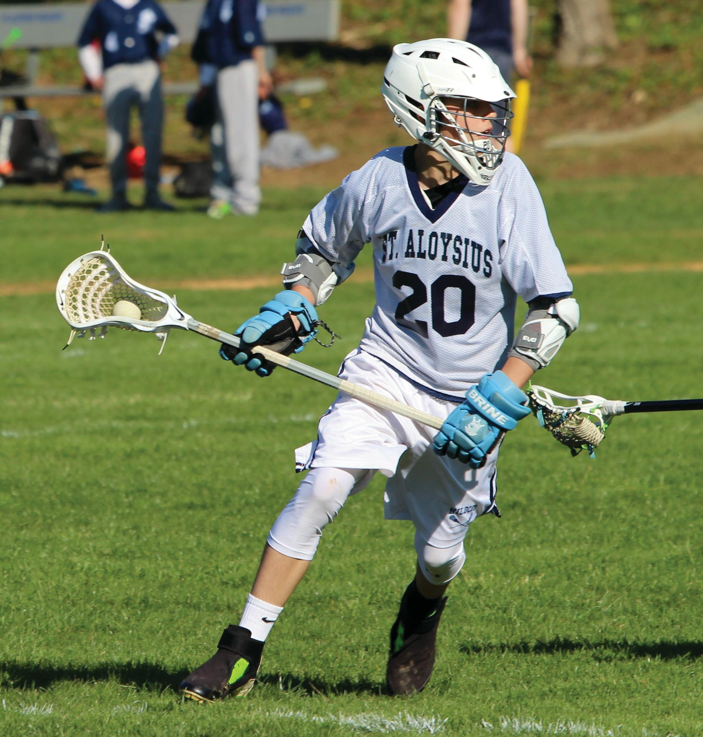 Child in lacrosse uniform and helmet holding a lacrosse stick