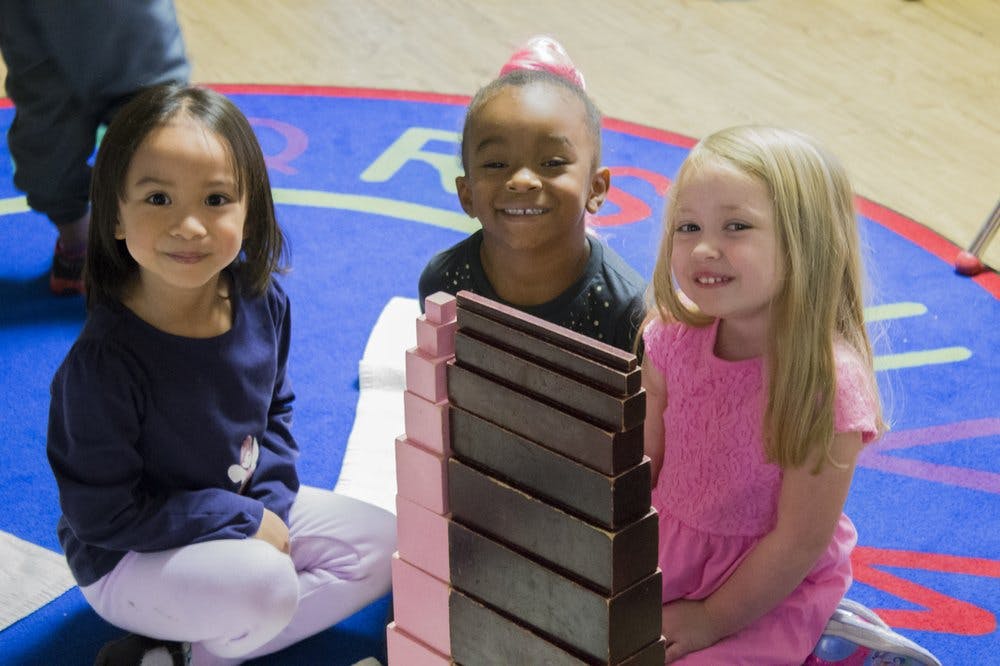 Three children sitting on a rug with blocks