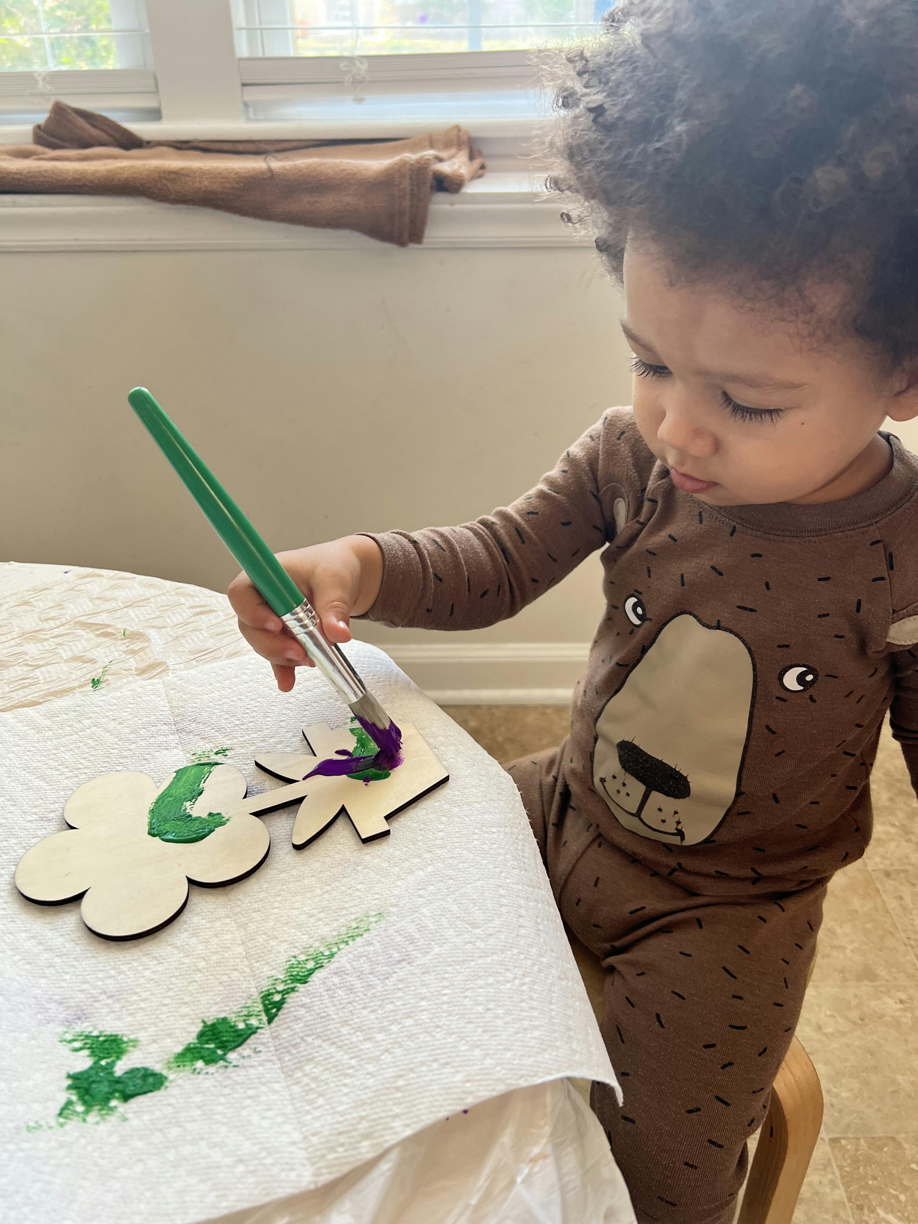 Child painting wooden cutouts with a paintbrush