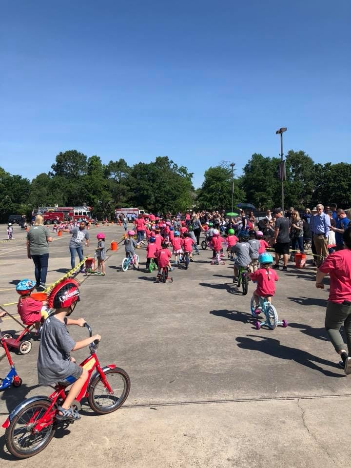 Many children on bicycles and balance bikes with adults in a paved area