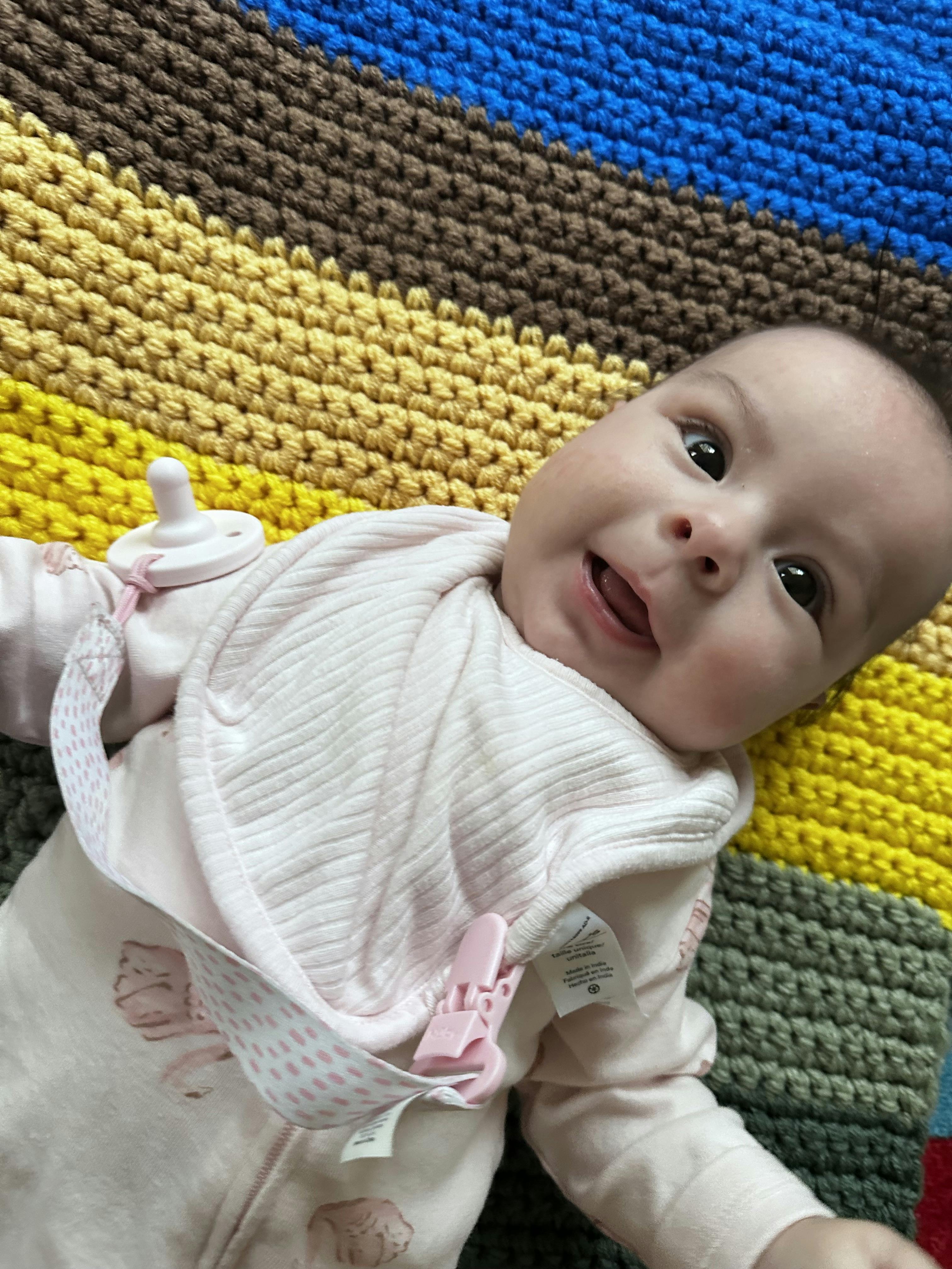 Child lying on a colorful striped blanket wearing a pink outfit and bib