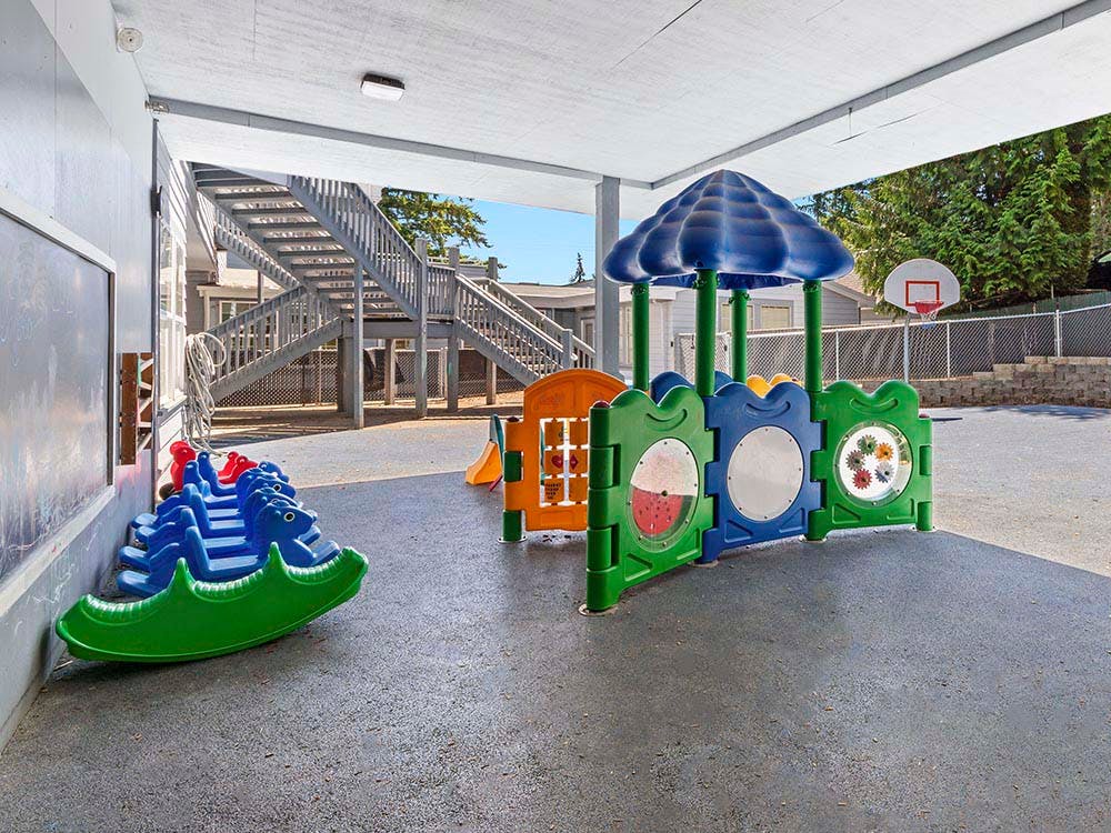 Covered outdoor playground with rock climbing steps, a small slide, and a basketball hoop