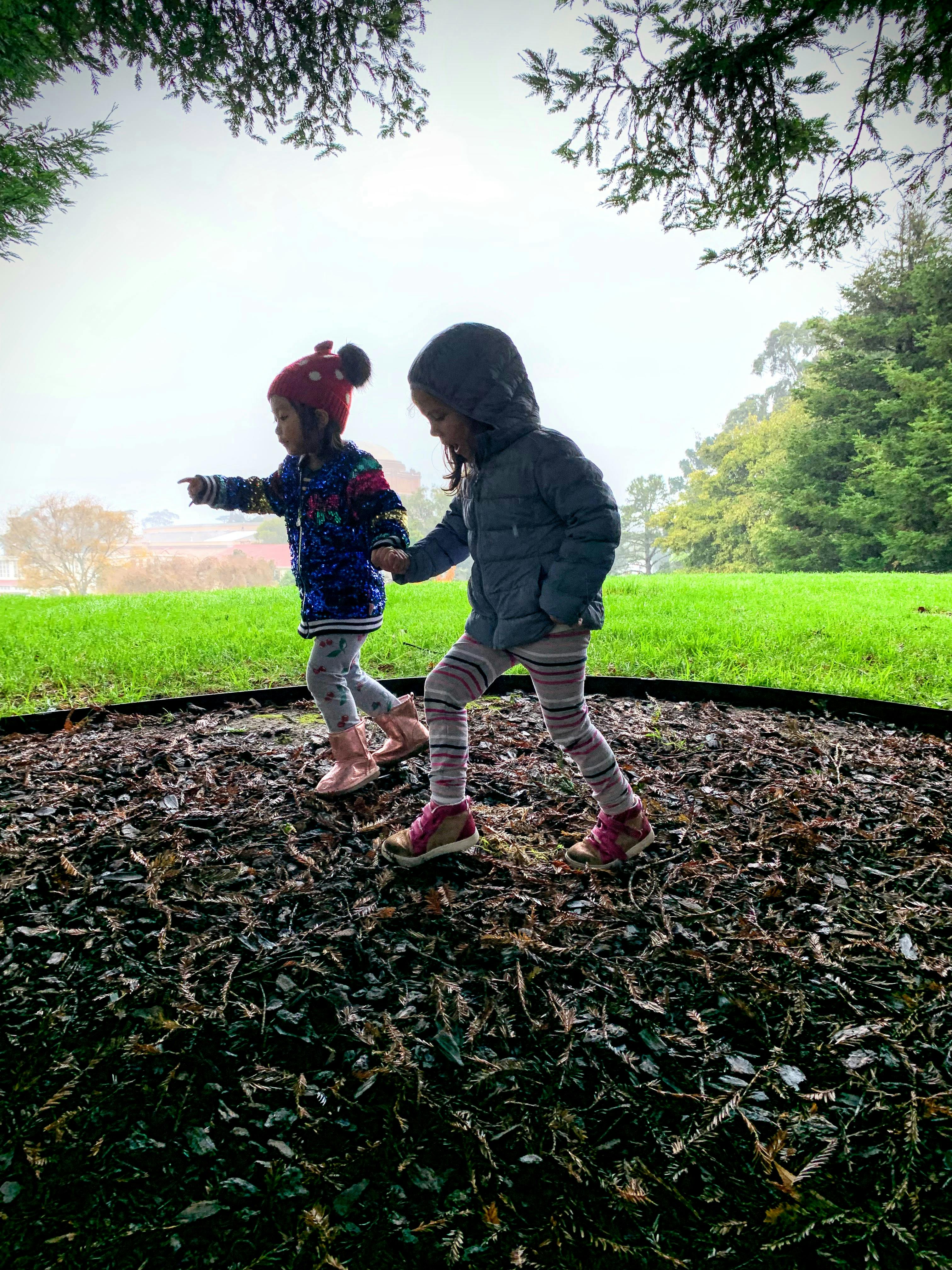 Two children walking on wood chips, one pointing