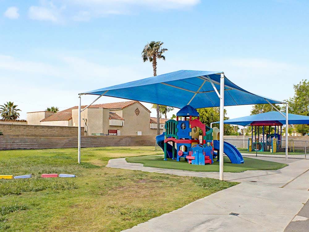 Playground with colorful play structures under blue shade canopies