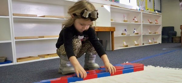 Child crouching on floor, arranging red and blue blocks
