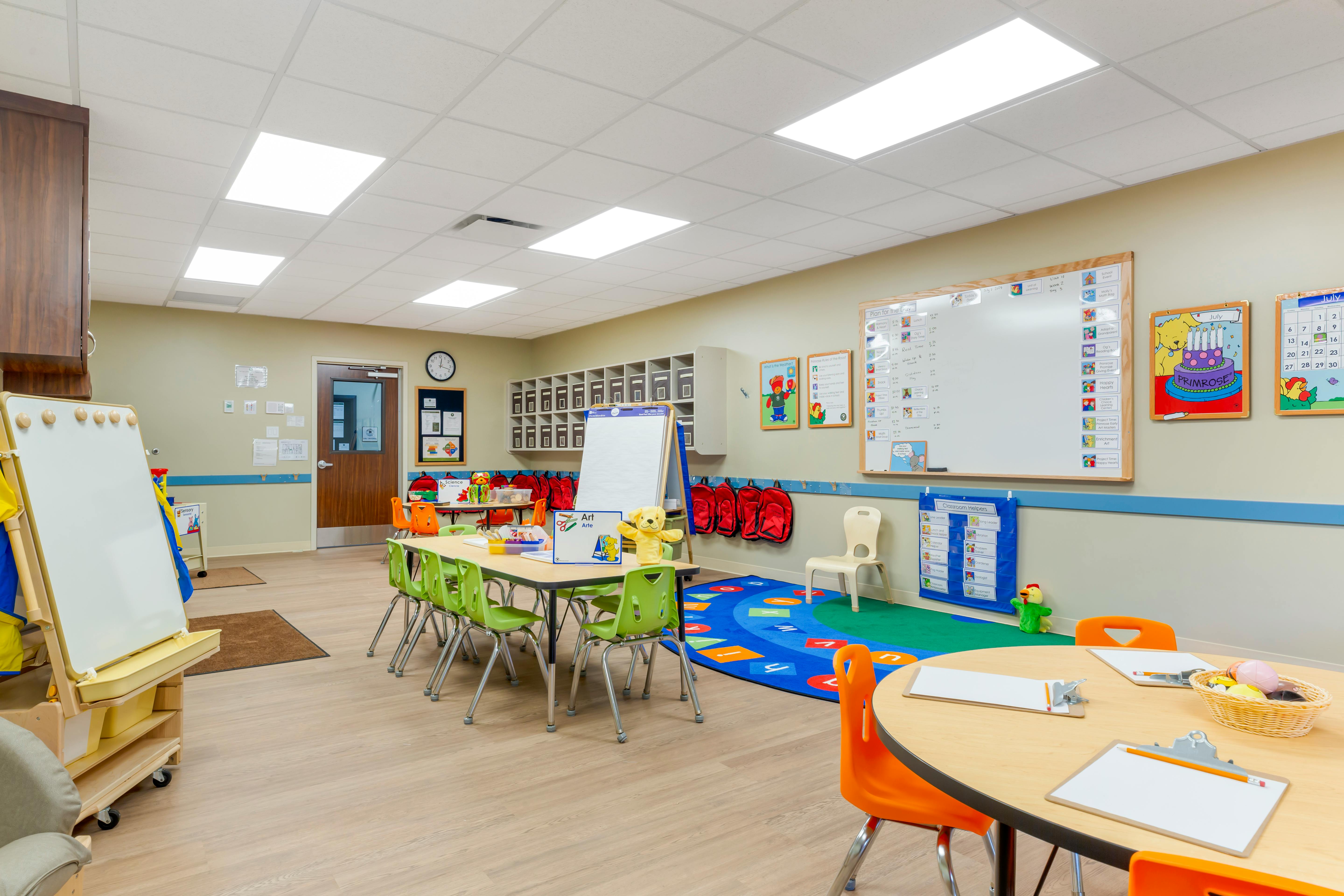Classroom with tables, chairs, colorful rug, and whiteboards