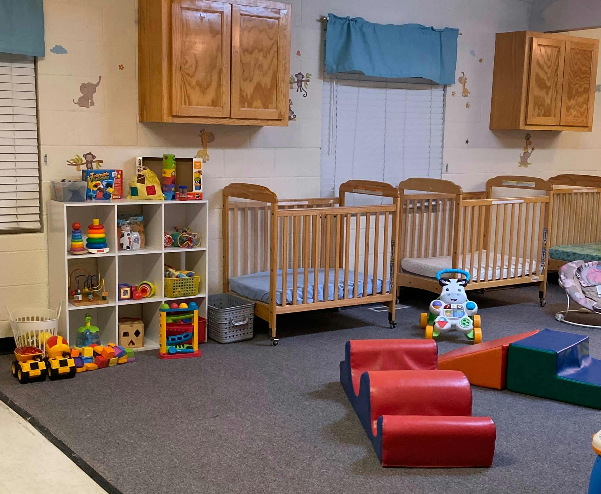 Nursery room with multiple cribs, a toy shelf, and soft play equipment