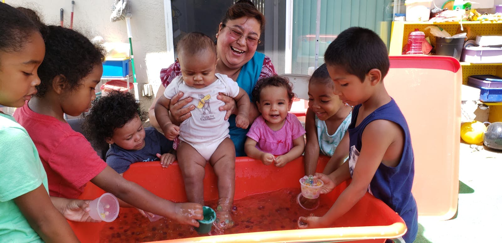 Adult and multiple children playing in a red water table