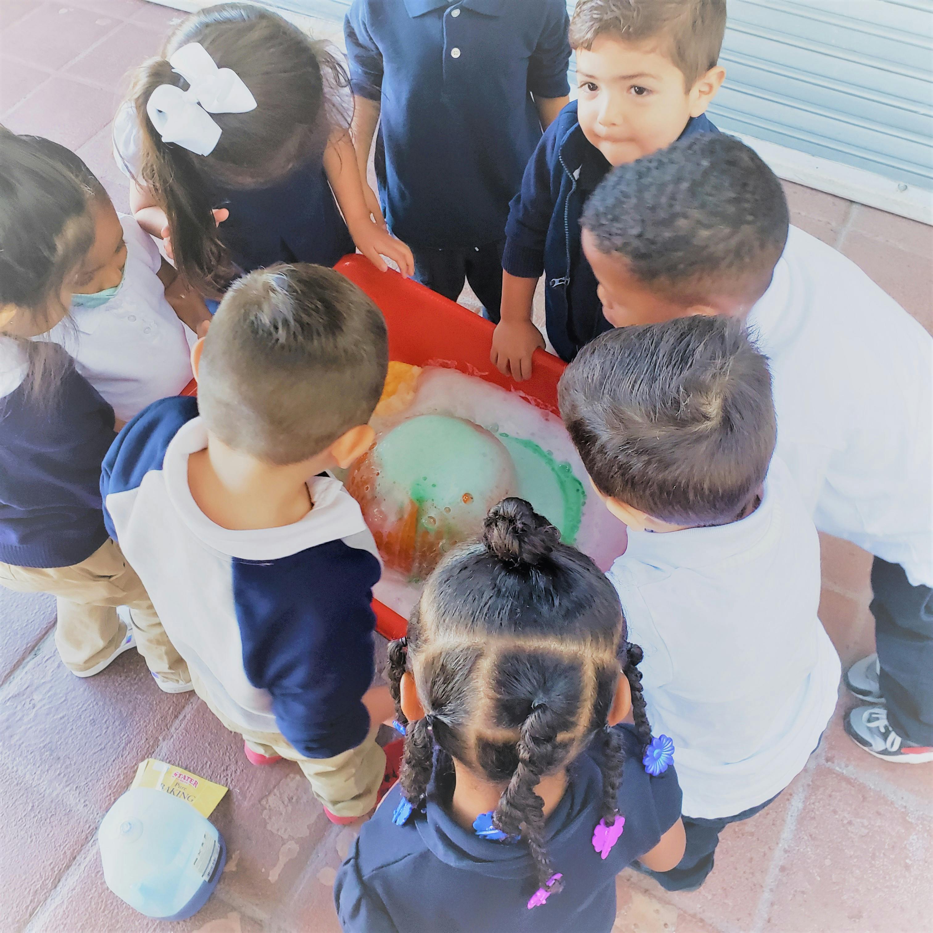 Children gathered around a container with a foamy substance