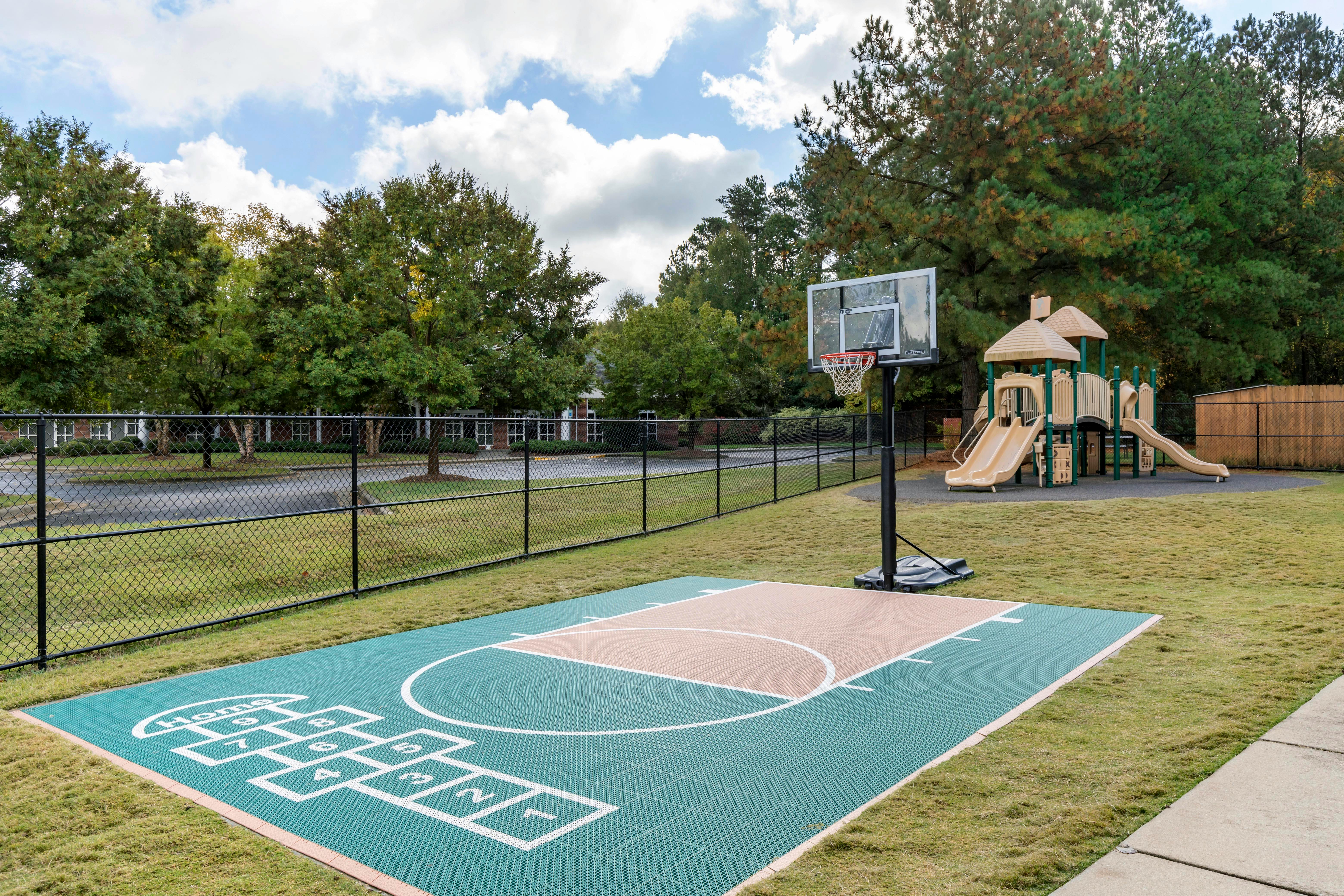 Basketball court and playground in a fenced grassy area