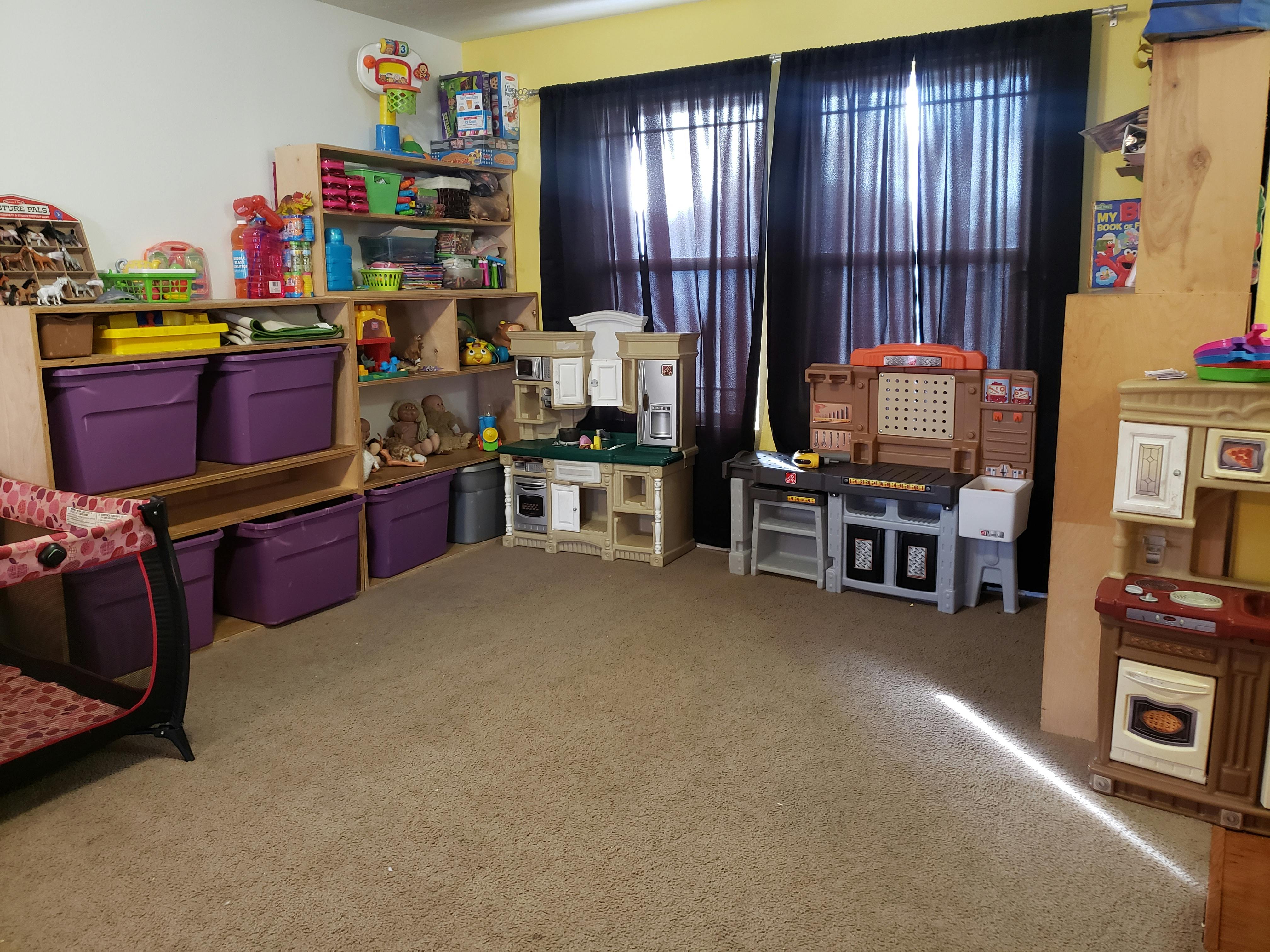 Playroom with shelves of toys, purple storage bins, and play kitchens